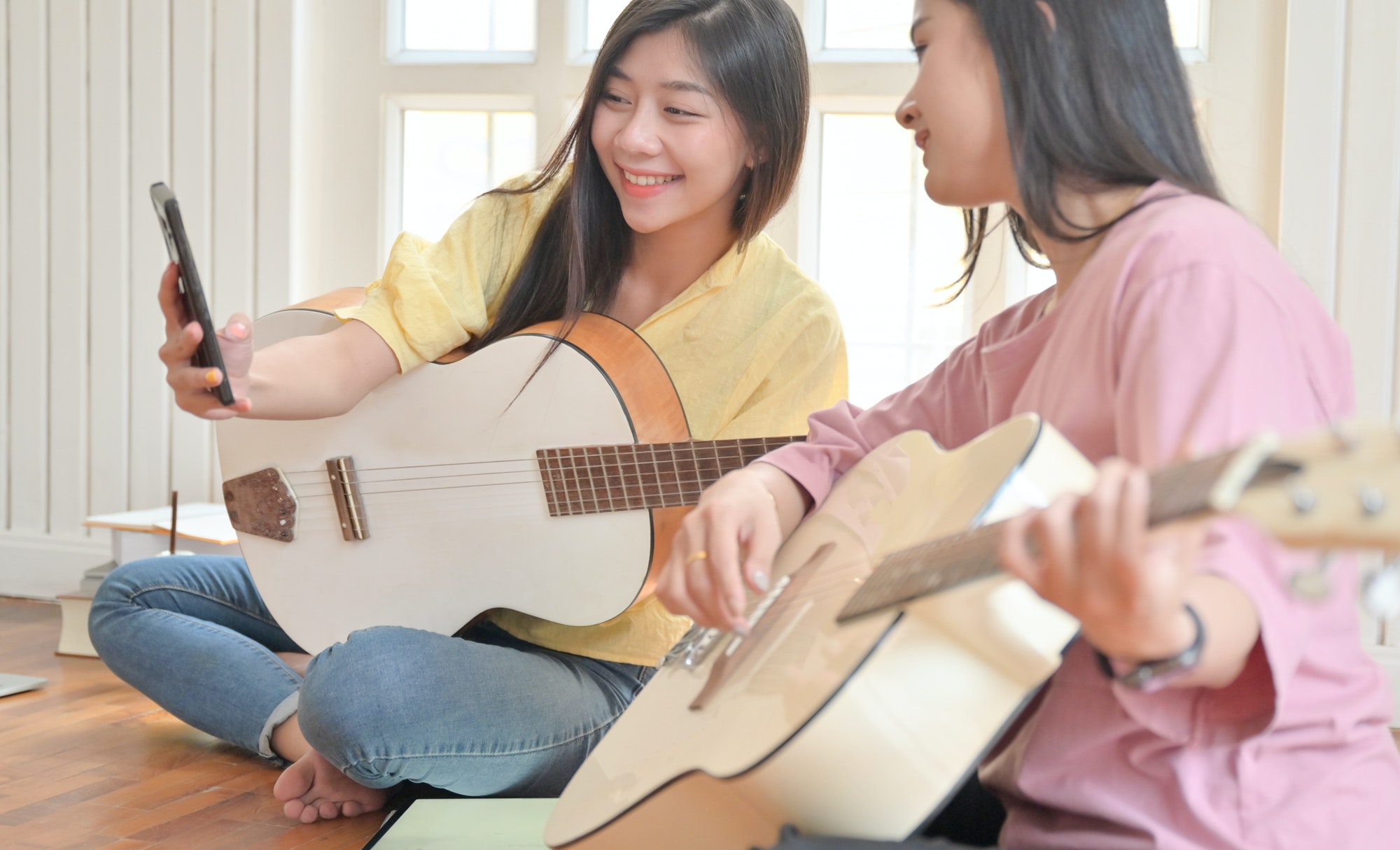 Teenage girls and friends playing guitar and using a smartphone video call.